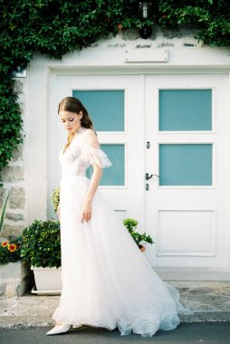Bride stands near the building overgrown with ivy. High quality photo
