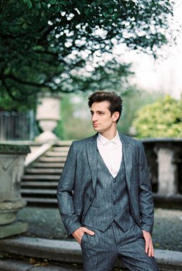 Man in a gray suit on stone steps in a green park. Portrait. High quality photo