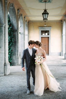 Bride with flowers hugs groom on the terrace with arches in the garden. High quality photo