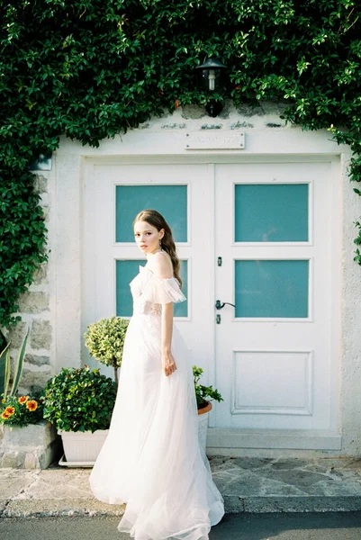Bride stands in front of the entrance to the building overgrown with ivy. High quality photo