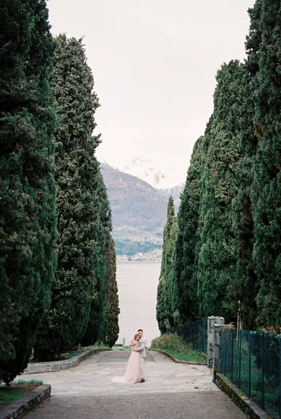 Groom Embraces Bride Park Tall Trees Backdrop Lake Como Italy —  Fotos de Stock