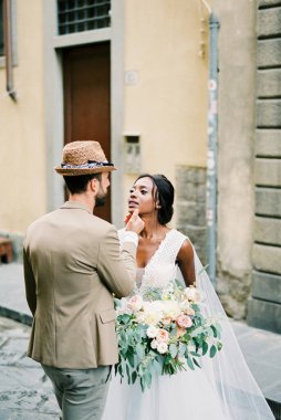 Groom touches bride chin while standing on the old street. High quality photo