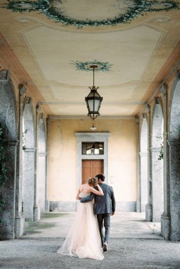 Bride and groom walk hugging along the terrace of an old villa. Back view. High quality photo