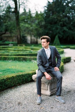Man in a suit sits on a stone flowerpot in the park. Como, Italy. High quality photo