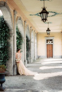 Bride in a beige dress with a bouquet on the arched terrace of an old villa. High quality photo