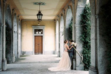 Groom hugs bride leaning against the arch of an old villa. Como, Italy. High quality photo