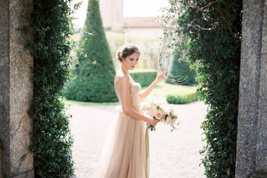 Bride with a bouquet stands against a wall covered with ivy. Lake Como, Italy. High quality photo