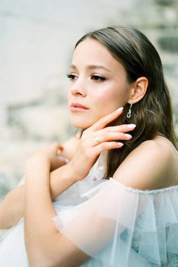 Bride in a white dress sits touching her chin with her fingers. High quality photo