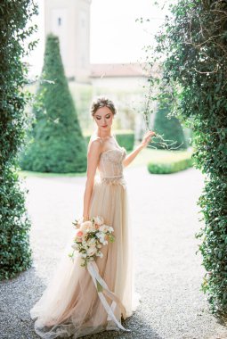 Bride with a bouquet stands in a park near a green bush. Como, Italy. High quality photo