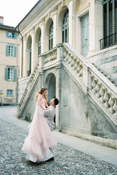 Groom lifts bride in his arms on the paving stones near the old building. Bergamo, Italy. High quality photo