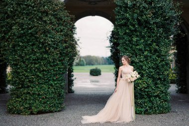 Bride with a bouquet stands near arches overgrown with green ivy. Como, Italy. High quality photo