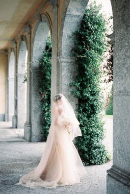 Bride in a veil stands half-turned near the column of old villa. High quality photo