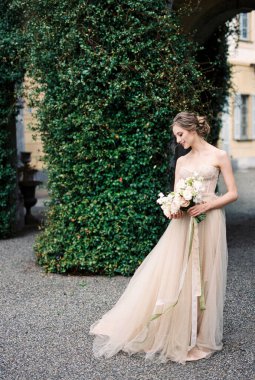 Bride stands near column overgrown with green ivy. Como, Italy. High quality photo