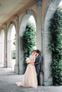 Groom hugs bride with a bouquet near the column of the old villa. High quality photo
