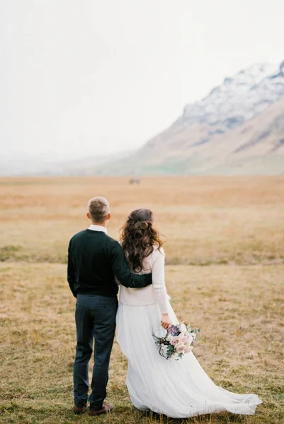 Sposo Abbraccia Sposa Con Bouquet Prato Asciutto Piedi Delle Montagne — Foto Stock