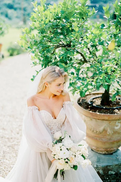 Bride with a bouquet of roses near a tree in a tub in the garden. High quality photo