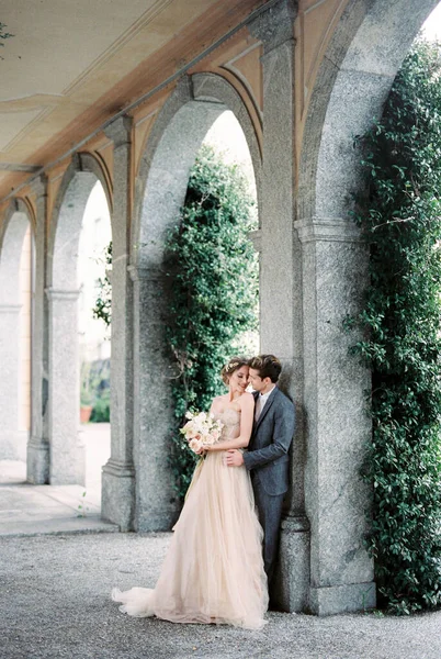 Groom hugs bride with a bouquet near the column of the old villa. High quality photo