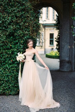 Bride with a bouquet stands near a column with green ivy. High quality photo