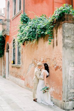 Groom hugs bride with a bouquet near the ancient building in Venice. High quality photo