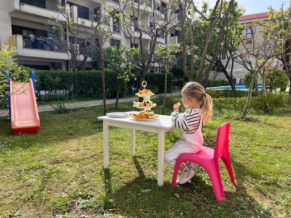 Little girl sits at a table with cakes on a stand. High quality photo