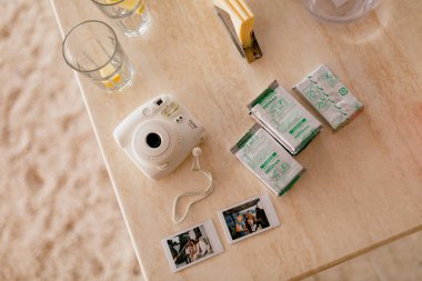 Fujifilm Instax Mini 8 white camera with spare film cartridges and instant photos lies on a wooden table. High quality photo