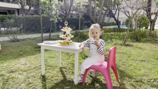 Little Girl Eats Piece Fruit Sitting Table Pink Chair High — Vídeo de Stock