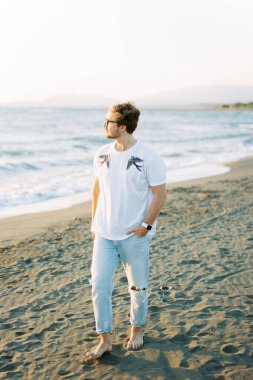 Young man walks barefoot on the beach and looks at the sea. High quality photo