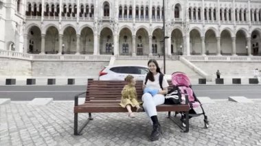 Mom feeds a little girl with a spoon near the building of the Hungarian Parliament. Budapest. High quality 4k footage