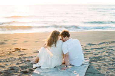 Man kissing woman shoulder while sitting on a blanket on the beach. High quality photo