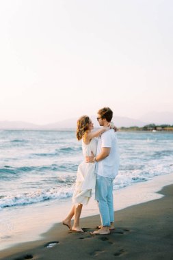Man hugs woman while standing on the beach. Side view. High quality photo