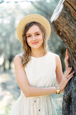 Girl in a straw hat stands near a tree in an olive grove. Portrait. High quality photo
