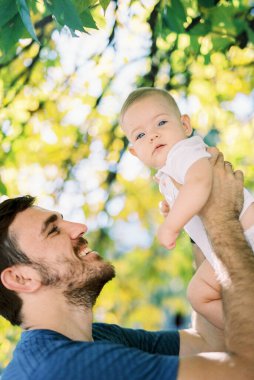 Dad raises a baby in a diaper over his head in his arms. High quality photo