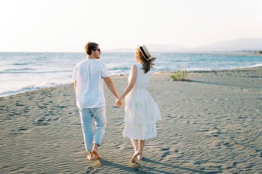 Man and woman walk along the beach, holding hands and looking at each other. High quality photo