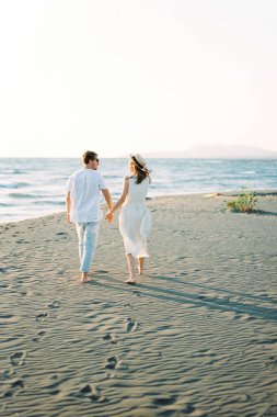 Man and woman walk along the beach leaving footprints in the sand. High quality photo