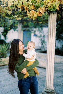 Smiling mother with a baby in her arms stands near the column. High quality photo
