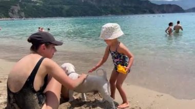 Mother and daughter pet the dog on the beach. High quality 4k footage