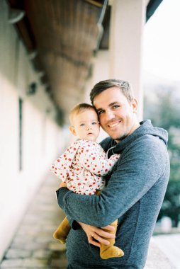 Smiling dad with a baby in his arms stands on the terrace. Portrait. High quality photo