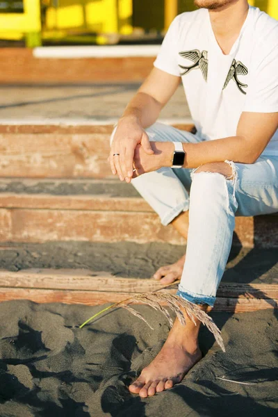 Young barefoot man sitting on the wooden steps. High quality photo