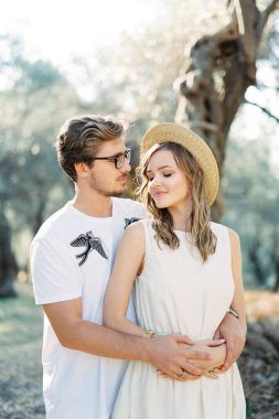 Man in glasses hugging woman in a straw hat from behind. High quality photo