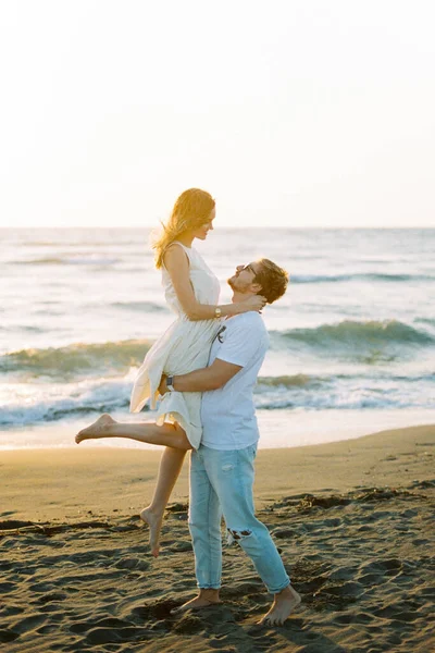 Man holding a woman in his arms on the beach near the sea. High quality photo