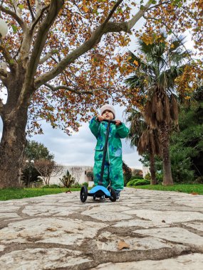 Small child is holding a scooter on a paved path in the park. High quality photo