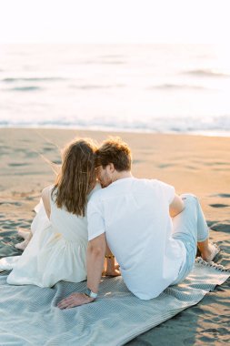 Man kissing woman shoulder while sitting on the beach. High quality photo