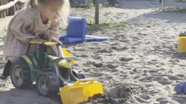 Little girl playing with a toy tractor with a bucket in the sandbox. High quality 4k footage