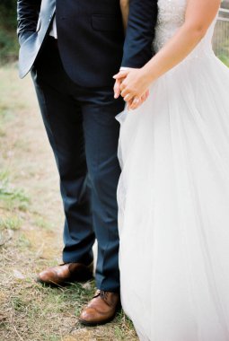 Groom holds bride by the hand standing on the grass. Close-up. High quality photo