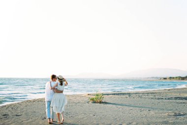 Man and woman stand embracing on the beach by the sea. Back view. High quality photo