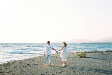 Man and woman walk holding hands on the beach by the sea. Back view. High quality photo