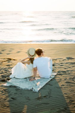 Woman in a hat sits on the beach leaning against the shoulder of a man. High quality photo