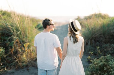 Woman in a straw hat stands next to a man on a country road. Back view. High quality photo