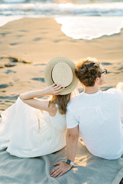 Woman sits on a blanket on the beach, leaning against a man. High quality photo