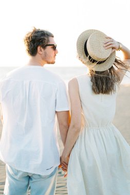 Woman holding a straw hat with her hand while standing hand in hand with a man. High quality photo